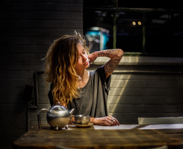 Žena s tetovaním na ruke sedí pri stole, na ktorom je kanvica s čajom.jpg